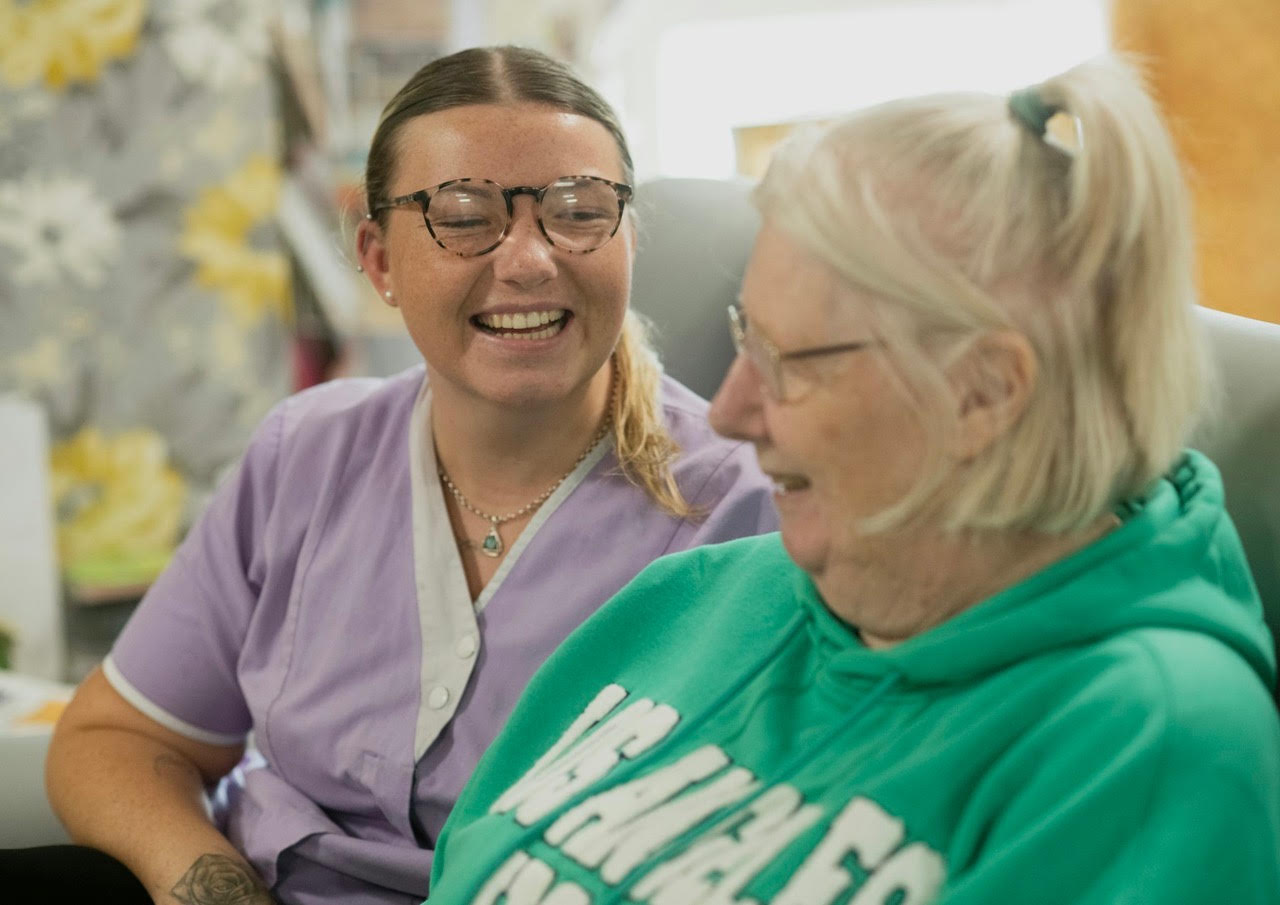 A nurse practitioner laughing with an older woman during a friendly visit
