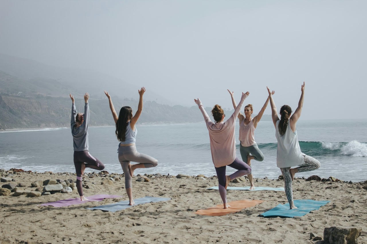 A group of women in a yoga class outdoors by the sea, arms raised